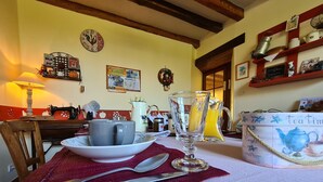 Une table à manger avec une théière, des tasses et un pichet, placée dans une cuisine chaleureuse aux poutres apparentes et ornée d’une horloge au mur.