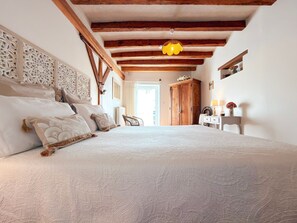 A bedroom with a large bed, wooden beams, a hanging light fixture, and a wardrobe.
