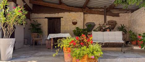 An outdoor patio with a wooden bench, potted plants, and a rustic stone wall.