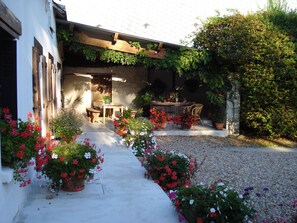 Une cour avec une pergola en bois, une table et des chaises, ainsi que des plantes en pot ornées de fleurs.