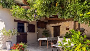 Une terrasse extérieure avec une table et des chaises, entourée de plantes en pot et d’un mur de pierres rustiques.