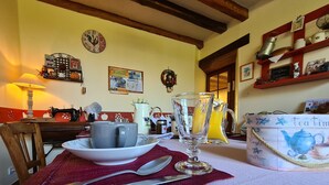 Une table à manger avec une théière, des tasses et un pichet, placée dans une cuisine chaleureuse aux poutres apparentes et ornée d’une horloge au mur.