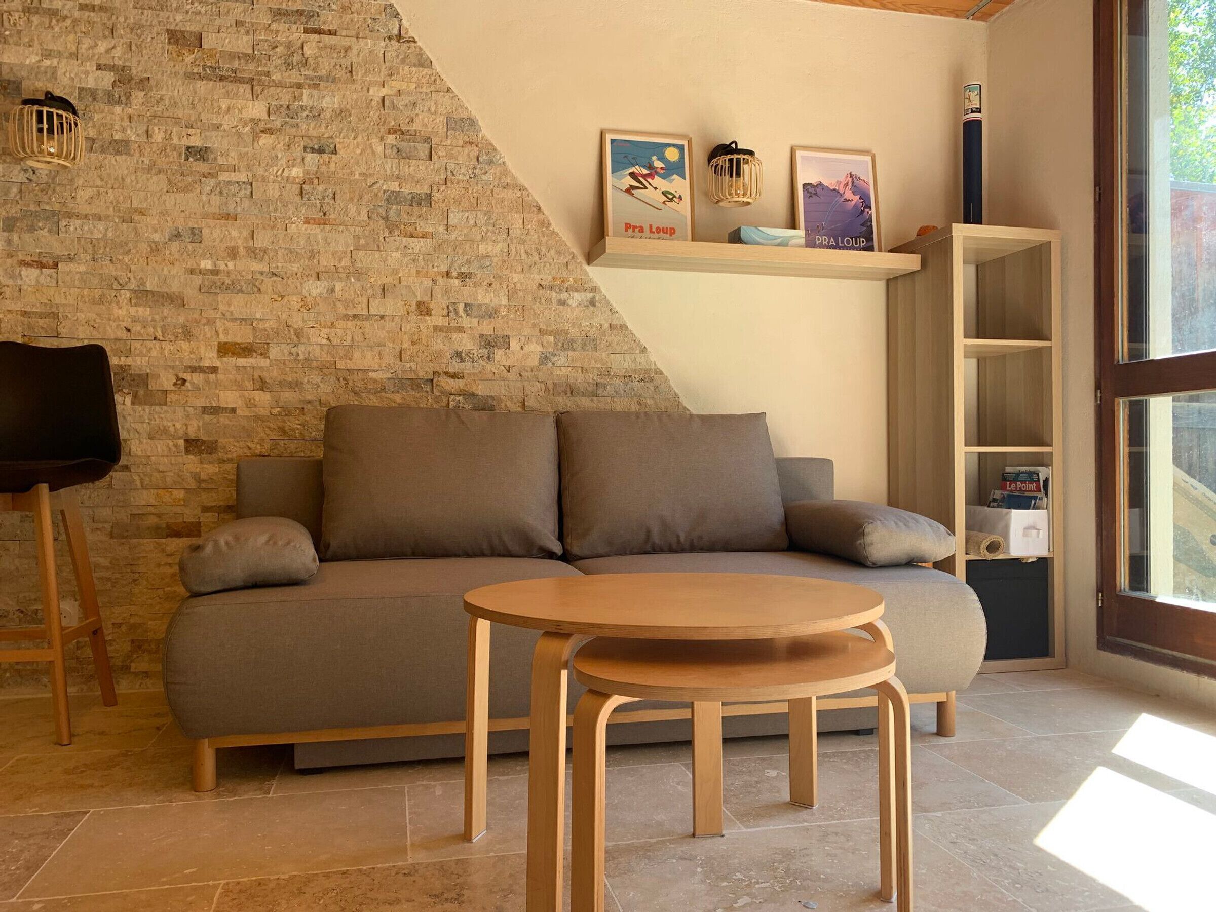 Una sala acogedora con pared de piedra, un sofá, una mesa de madera y una estantería con cuadros enmarcados.