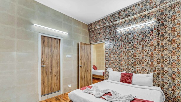 A hotel room with a wooden floor, a bed with white bedding and red accents, a wooden wardrobe, and a patterned tile wall. - Season4 Residences 1-BHK furnished appt (Chennai)