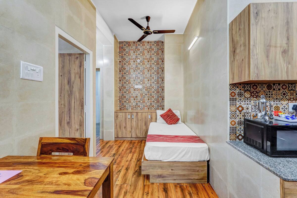 A compact room with a bed, a small table, a ceiling fan, and a microwave.