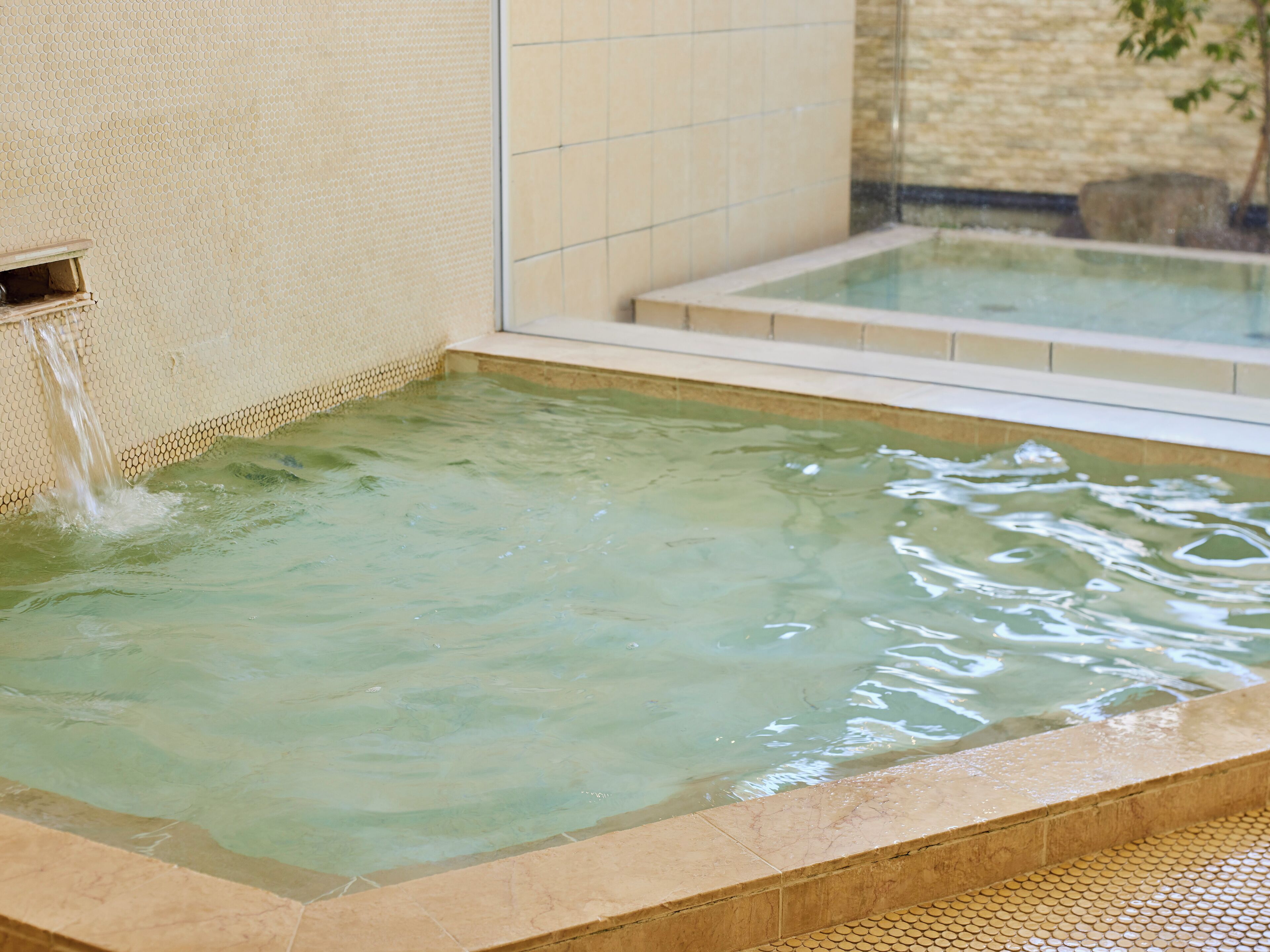 Una piscina de hidromasaje con agua cristalina, pared de azulejos y borde de piedra.