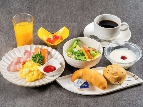 A breakfast setting with plates of food, a glass of orange juice, a cup of coffee, and a bowl of salad. - Matsuura City Hotel (Matsuura)