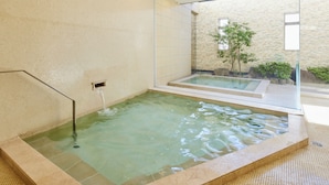 A spa area with a hot tub, a tiled wall, and a view of a garden through a glass partition.