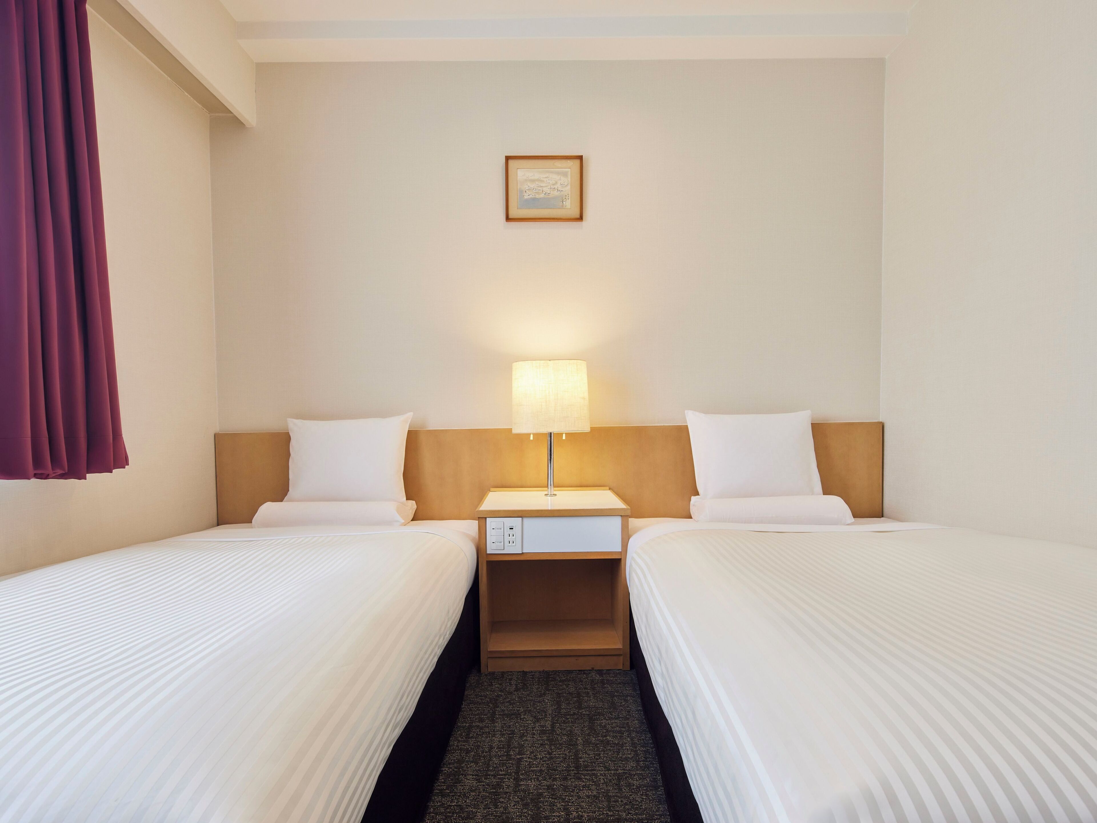 A hotel room with two beds, a nightstand, a lamp, and a framed picture on the wall.