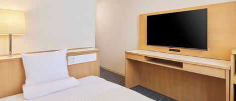 Habitación de hotel con una cama, una mesita de noche con lámpara, un televisor en una pared de madera y un pequeño escritorio con una silla.