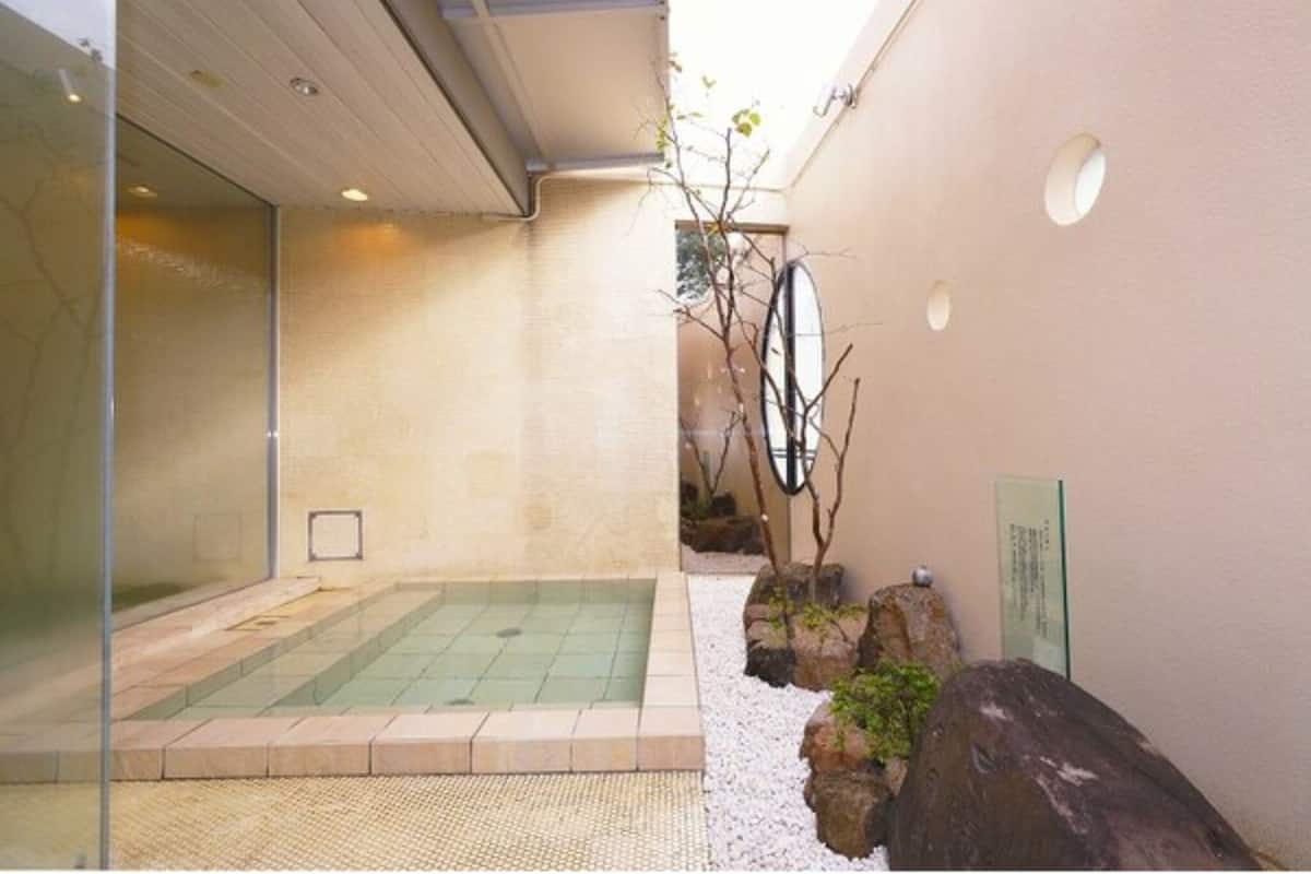 Un área de spa con un jacuzzi, un pequeño jardín con rocas y un árbol, y una pared de vidrio.