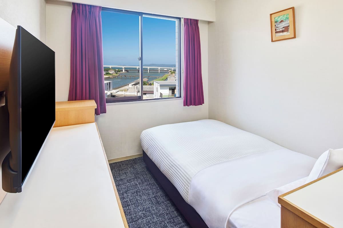 A hotel room with a bed, a desk, a TV, and a window with curtains.
