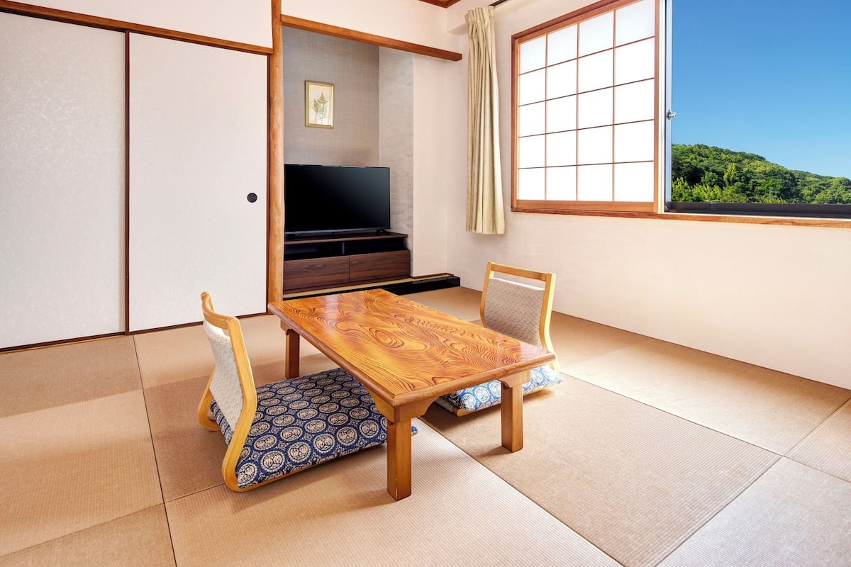 A traditional Japanese room with tatami flooring, a low wooden table, two chairs, a television, and a sliding door.