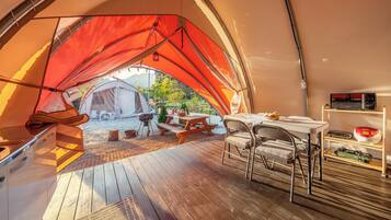 A tent with a picnic table and chairs, a grill, and a shelf with items.