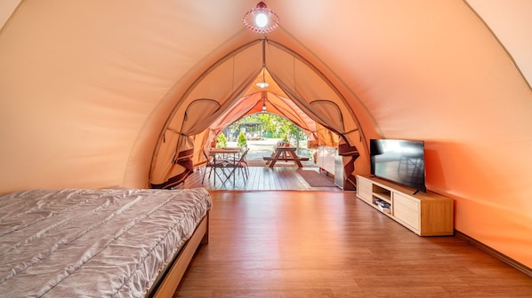 Une tente confortable équipée d’un lit, d’un téléviseur et d’un coin repas avec une table et des chaises.
