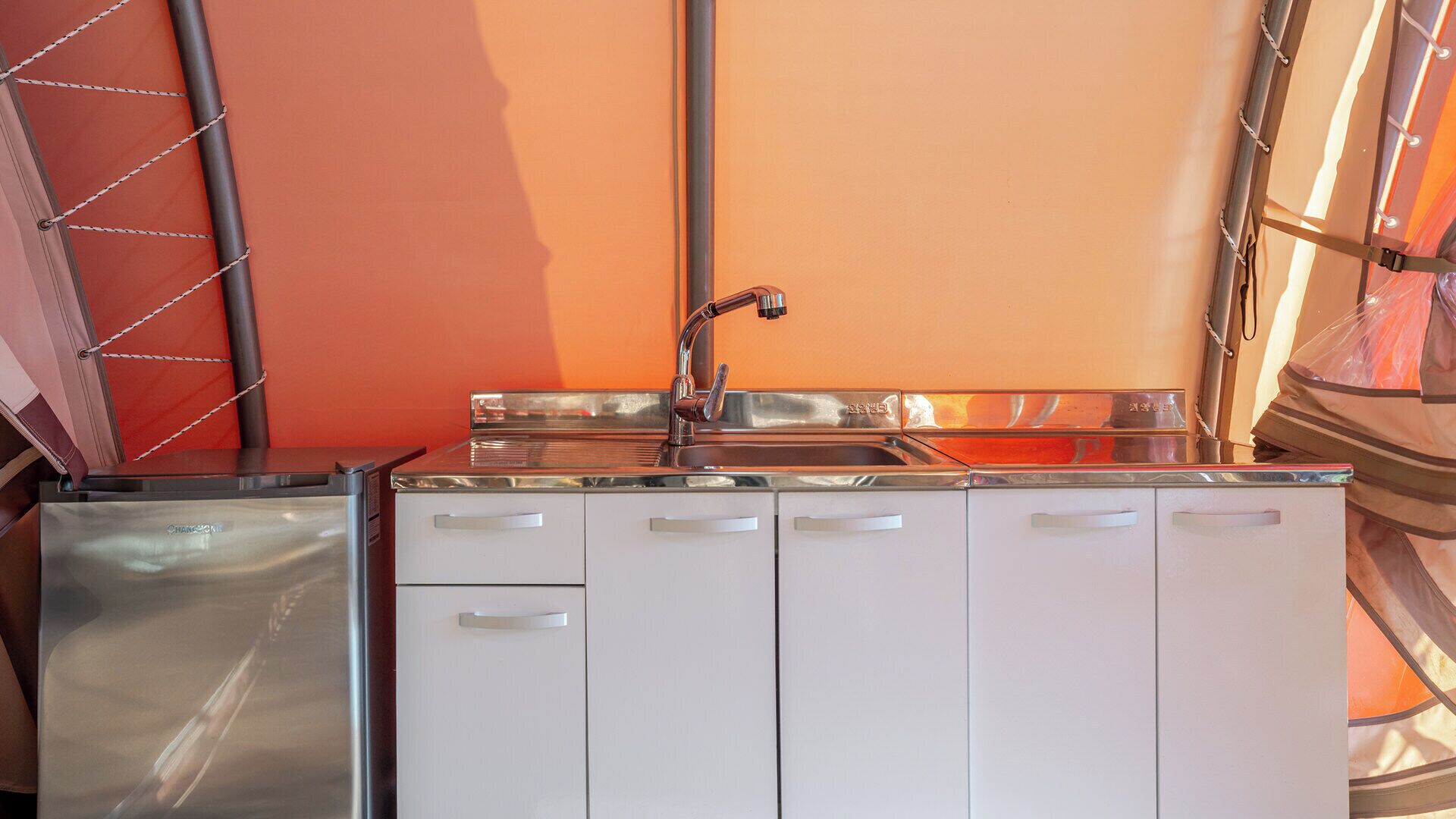 A compact kitchen with a stainless steel sink, white cabinets, and a red wall.