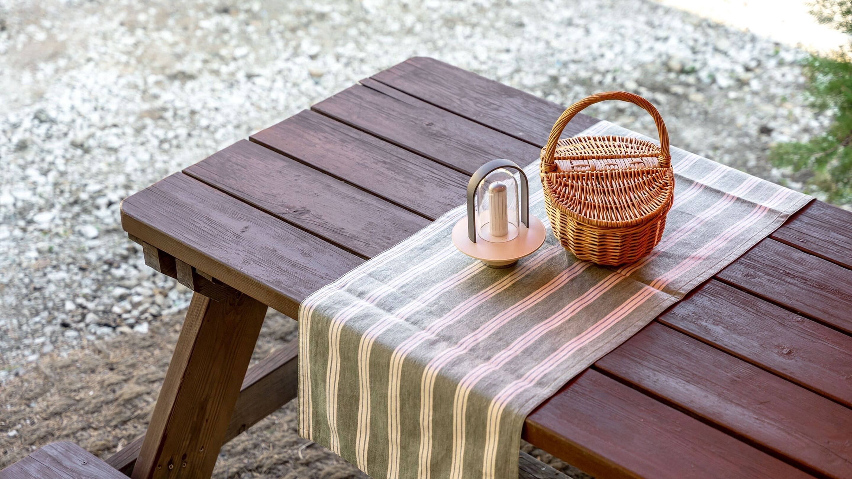 Un tavolo da picnic in legno con tovaglia a righe, un cesto in vimini e un bollitore in metallo.