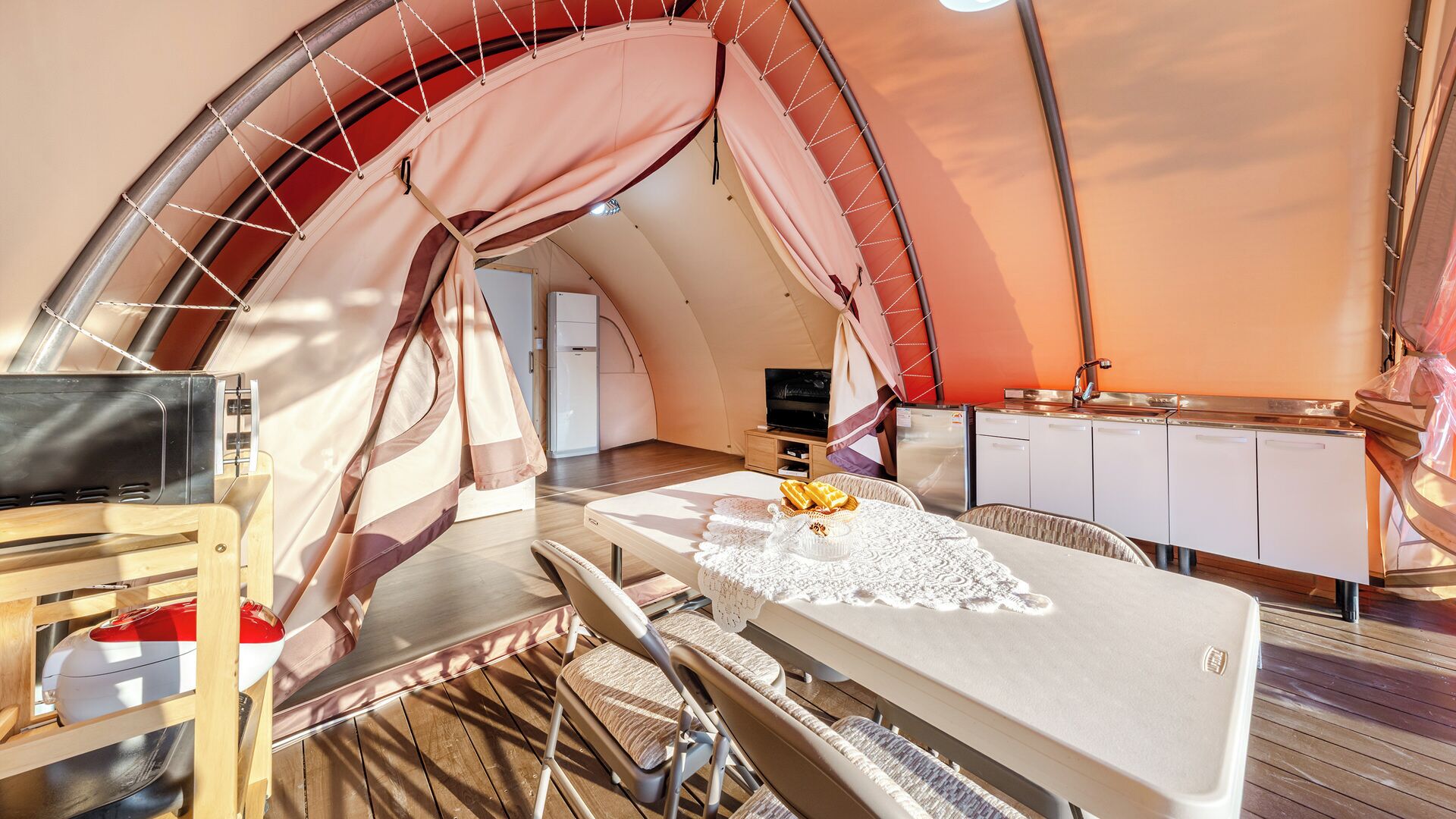 A compact, modern tent-style accommodation with a kitchenette, a flat-screen TV, and a dining area with a table and chairs.