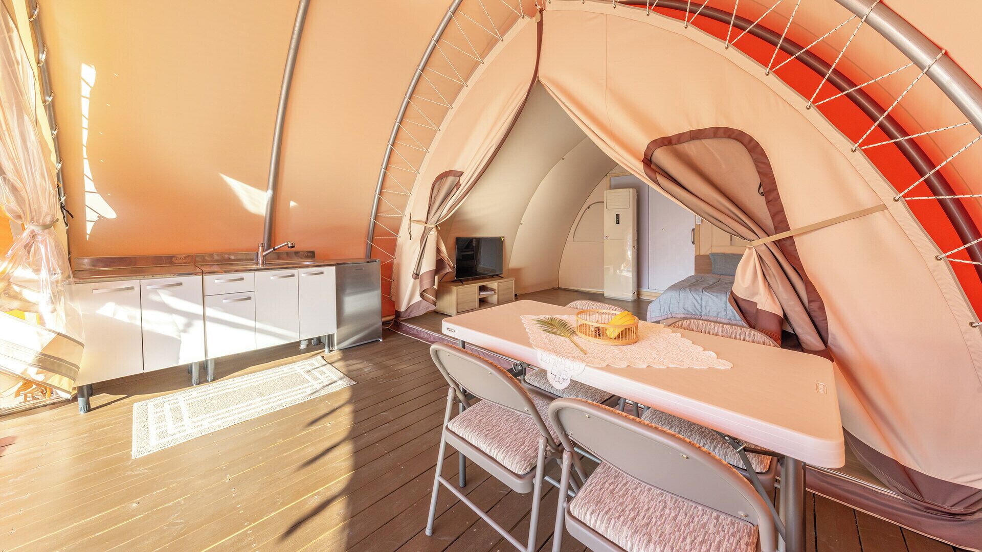 A compact, well-lit tent with a kitchenette, a dining area, and a bed.