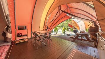 Alojamiento con carpa, una terraza de madera, una mesa con sillas, una parrilla y un televisor.