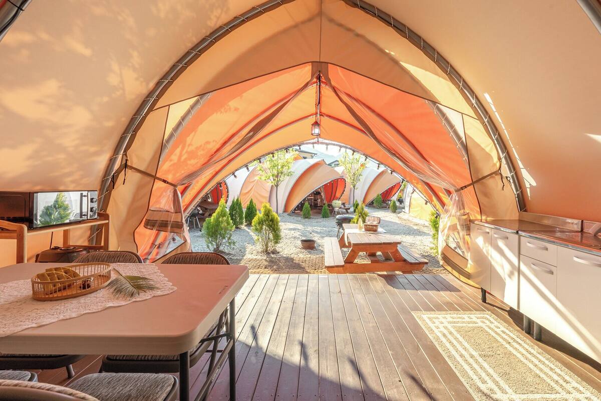 Alojamiento con carpa, zona de comedor, cocina y asientos exteriores.