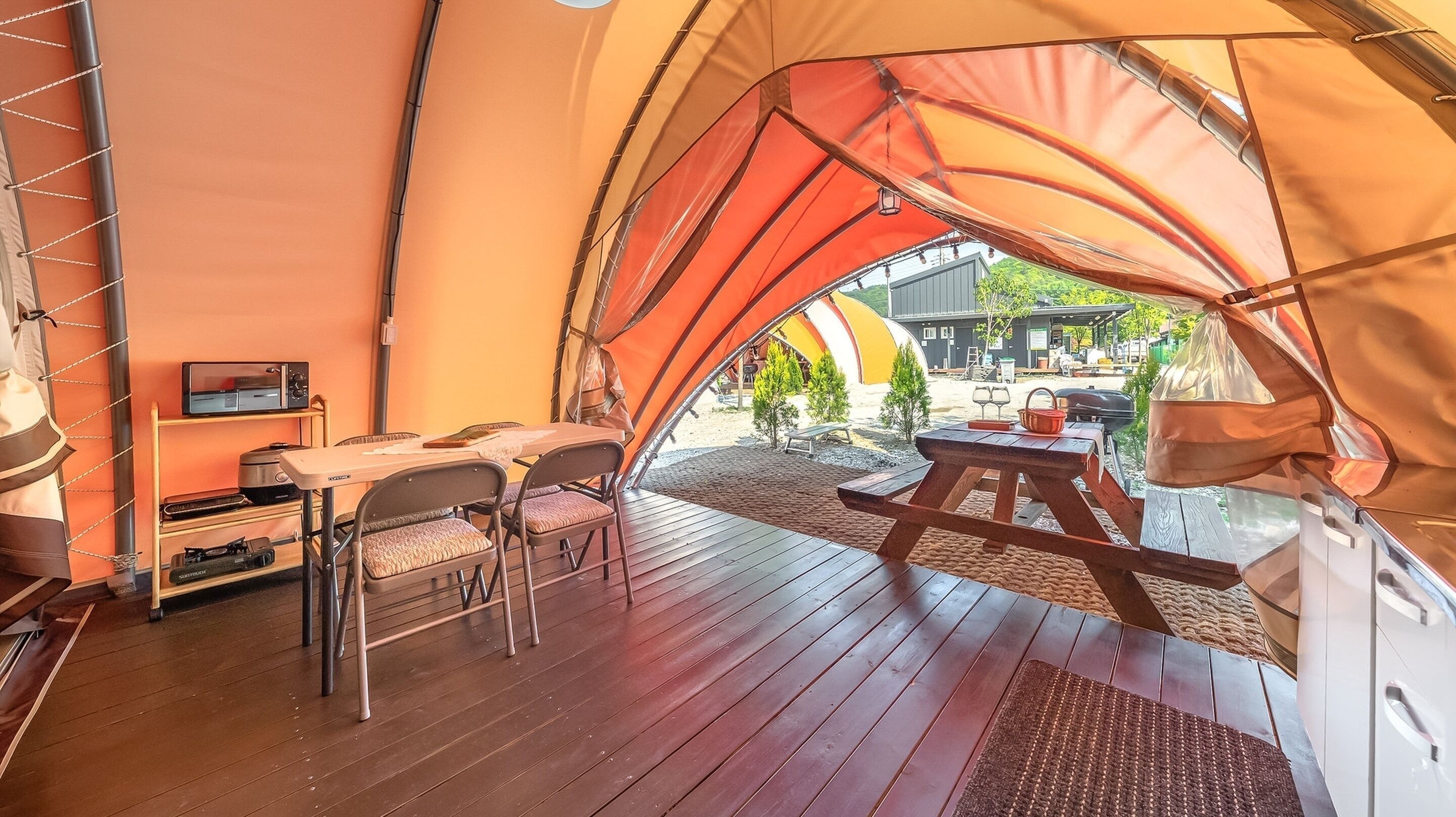 Une tente dotée d’une terrasse en bois, d’une table, de chaises et d’un petit téléviseur.