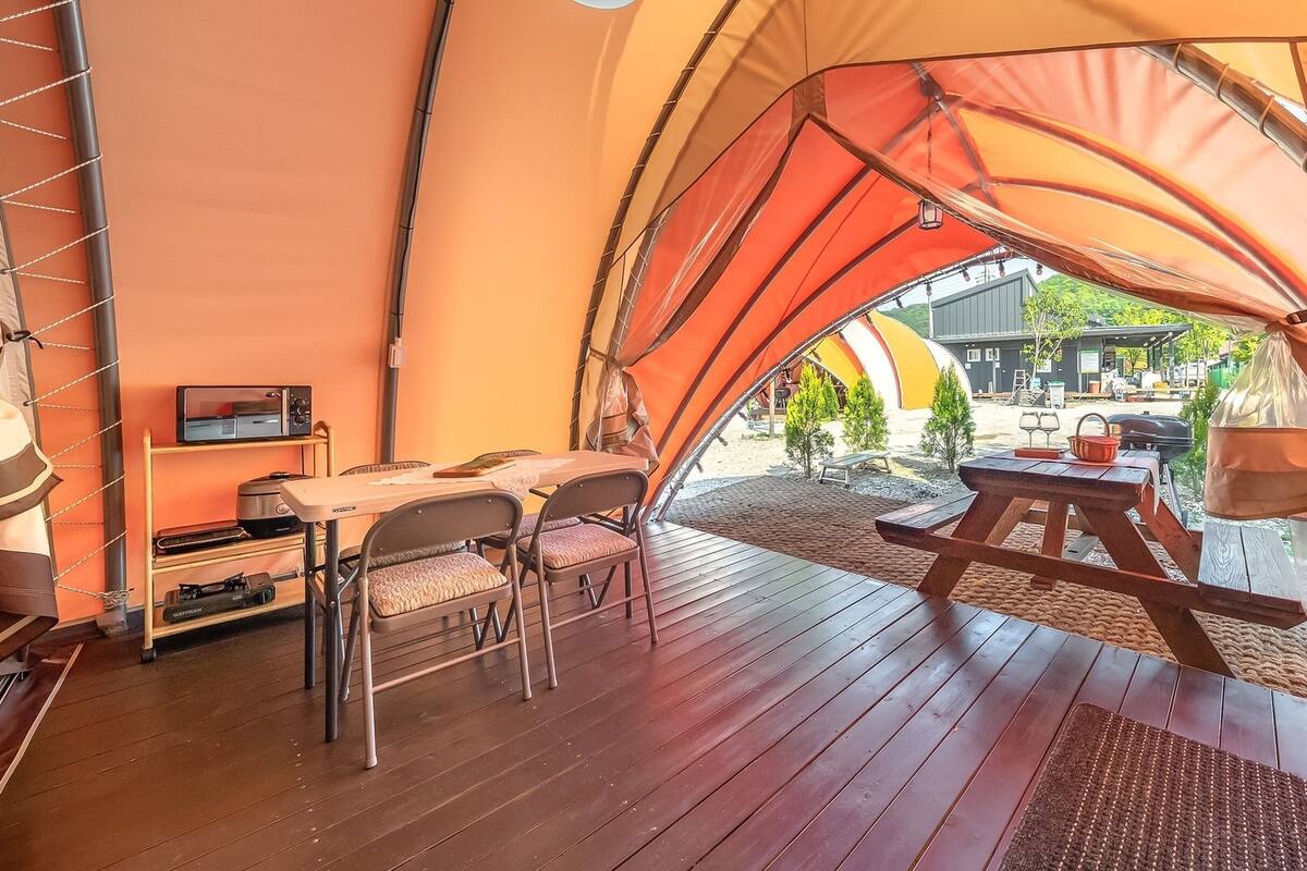 Una carpa con una terraza de madera, una mesa, sillas y un televisor pequeño.