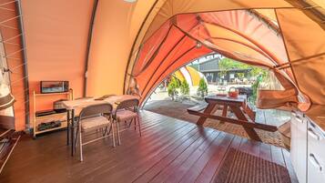 A tent with a wooden deck, a table, chairs, and a small TV.