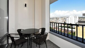 A balcony with a table and chairs, a view of a cityscape, and a railing.
