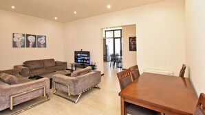 A modern living room with a sofa set, a coffee table, and a TV. There is a dining table with chairs in the background.