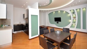 A modern kitchen with a built-in oven and microwave, a dining area with a table and chairs, and a living space with a TV mounted on the wall.