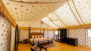 A tent-style room with a four-poster bed, a small table, a chair, and a television. - Talai Desert Camp (Jaisalmer)
