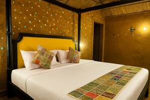 Ein Bett mit weißer Bettdecke, zwei Zierkissen, einem Holzkopfstück und einer Wand mit strukturierter Oberfläche und kleinen Löchern.