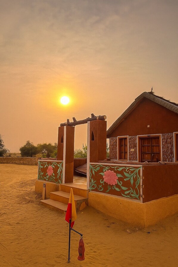 A desert house with a wooden door and windows, a small porch, and a flagpole with a flag. - Talai Desert Camp (Jaisalmer)