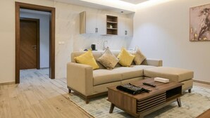 A modern living room with a beige sofa, wooden coffee table, and a kitchen area with cabinets and a countertop. - Tiara hotel (Jeddah)