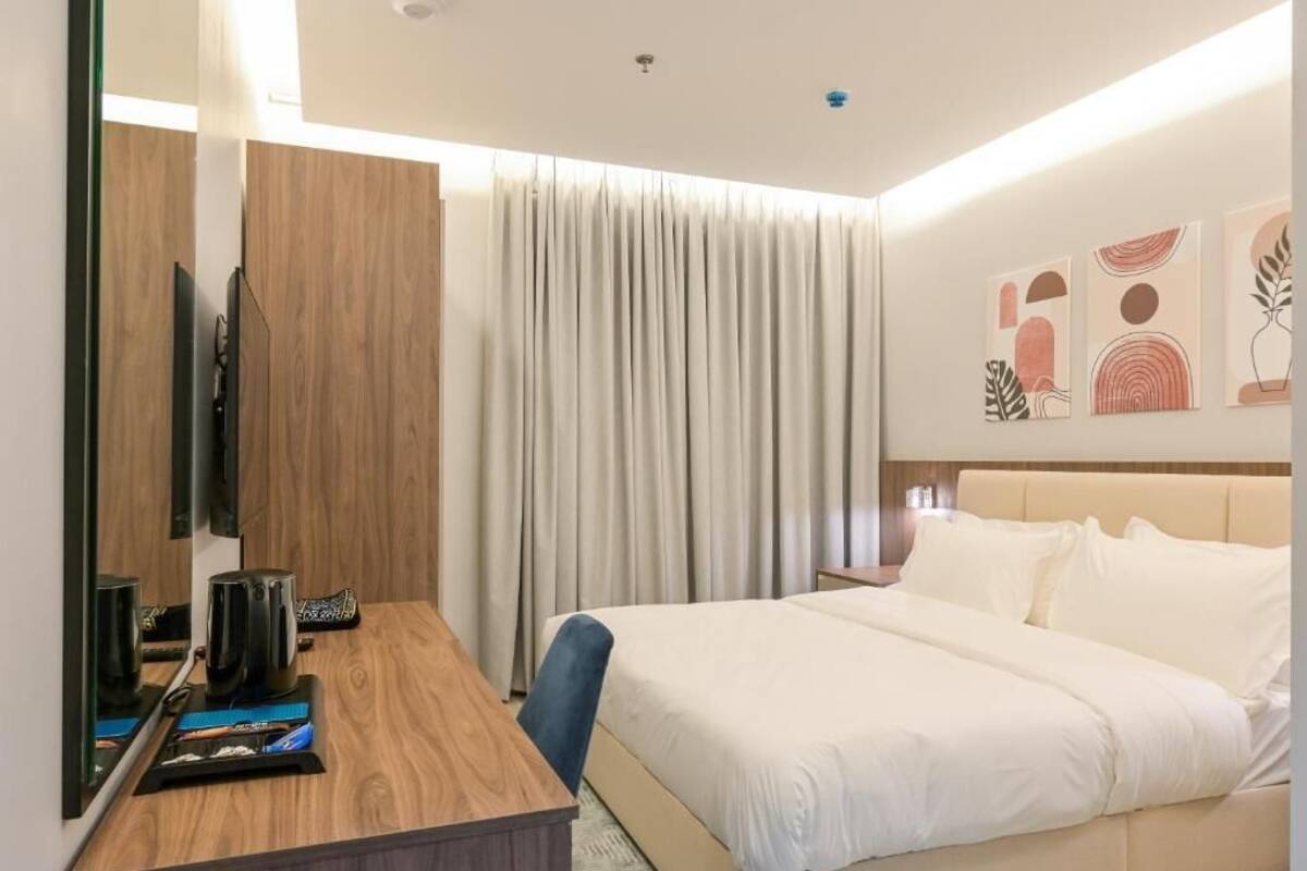 Une chambre d’hôtel avec un lit, un bureau avec un ordinateur, un miroir et une fenêtre avec des rideaux.
