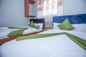 A hotel room with two beds, each with white linens and green accents, a wooden headboard, and a nightstand with a water bottle.