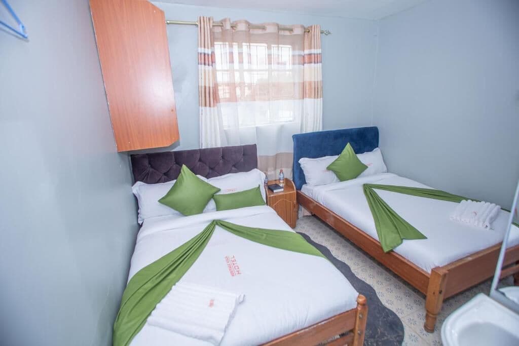 A hotel room with two beds, each with green and white bedding, a wooden headboard, and a window with striped curtains.