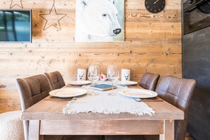 Une table à manger en bois, avec quatre chaises, un set de table blanc et une horloge au mur.