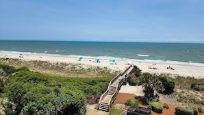 A beach with a wooden boardwalk leading to the shore, clear skies, and calm sea. - Heron Marsh Villa 78 (Pawleys Island)