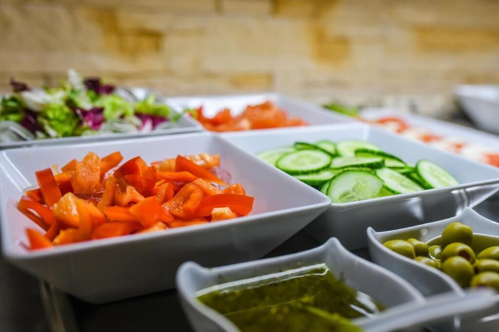 A variety of fresh vegetable platters including carrots, cucumbers, and olives, arranged on a table.