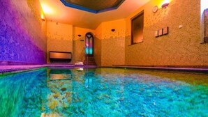 A clear indoor swimming pool with a tiled floor, a staircase leading to a higher level, and a wall with a clock and light switches. - Pensjonat Fitness i Spa Gregor (Zielona Góra)