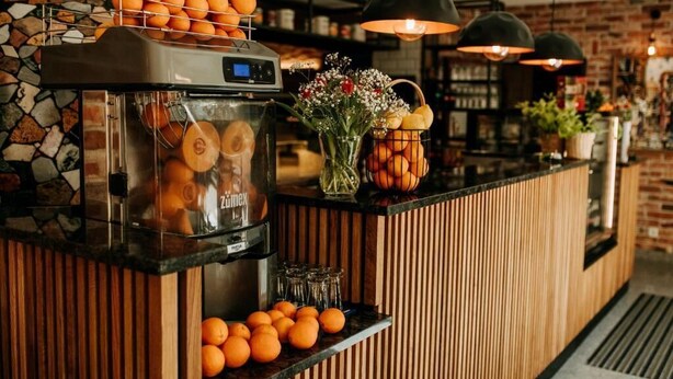 A breakfast bar with a juice dispenser, oranges, and a vase of flowers. - Pensjonat Fitness i Spa Gregor (Zielona Góra)