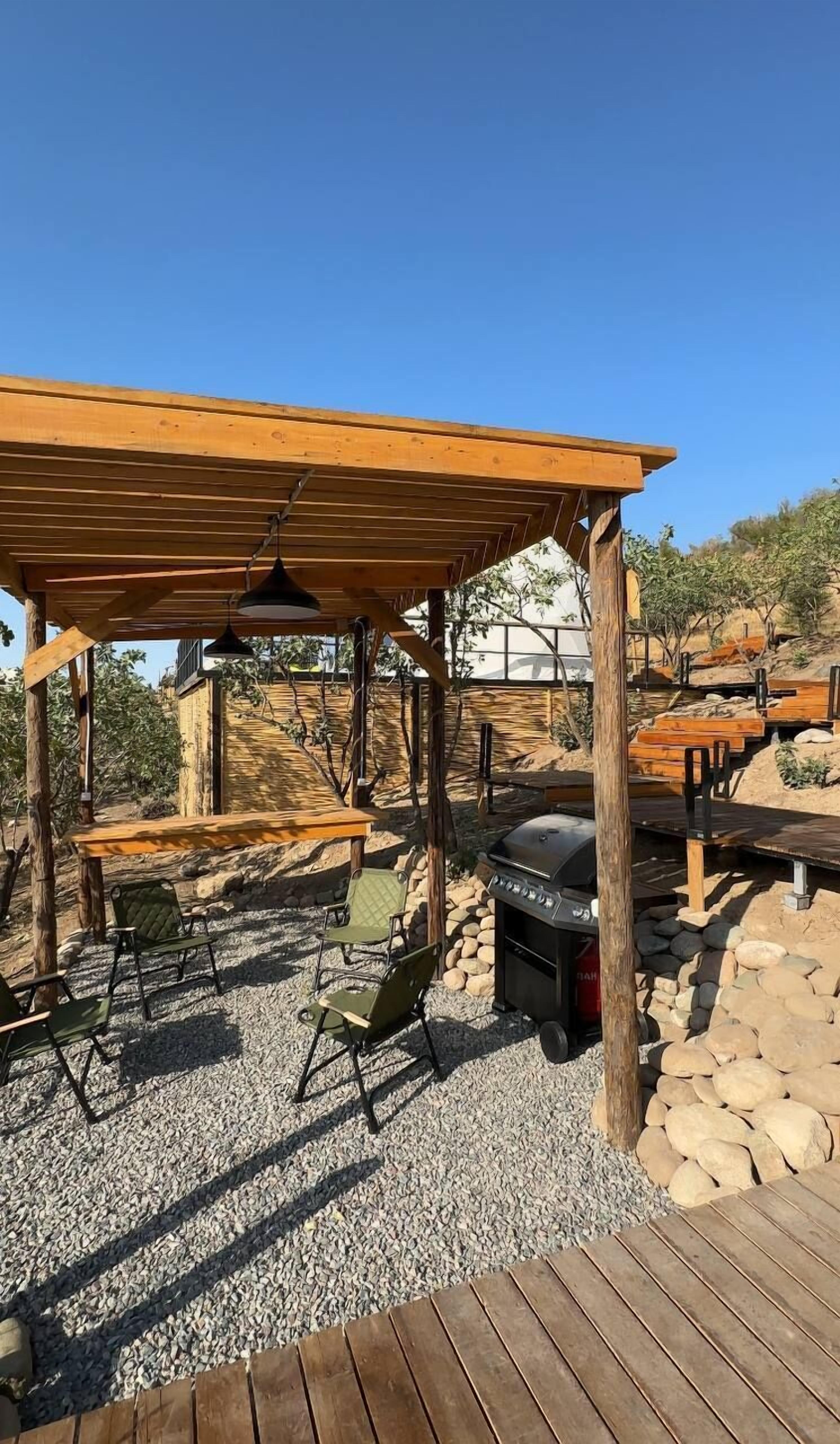 Un patio exterior con una pérgola, mobiliario y una parrilla.