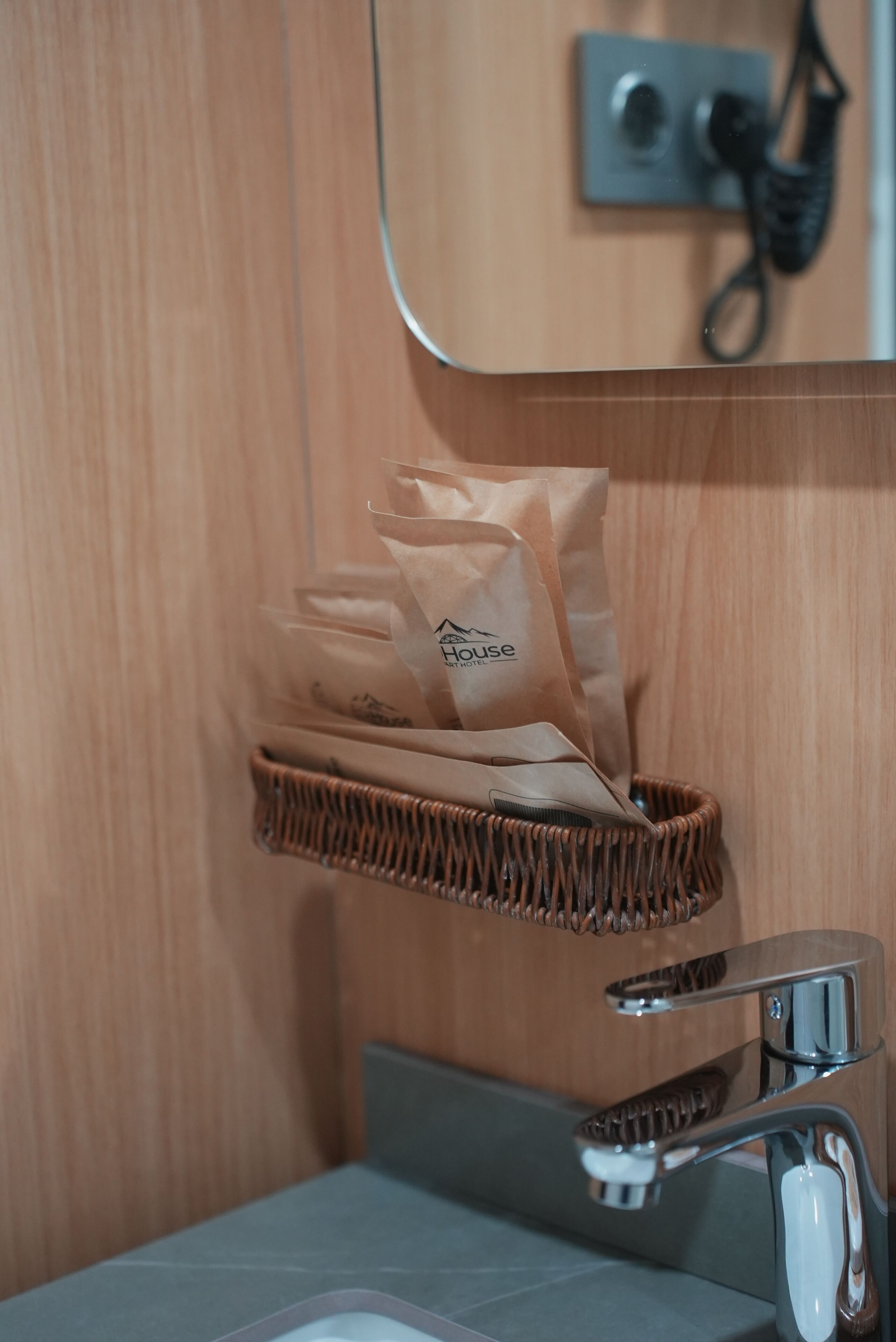 A bathroom with a wicker basket holding a paper bag, a mirror, and a telephone mounted on the wall.