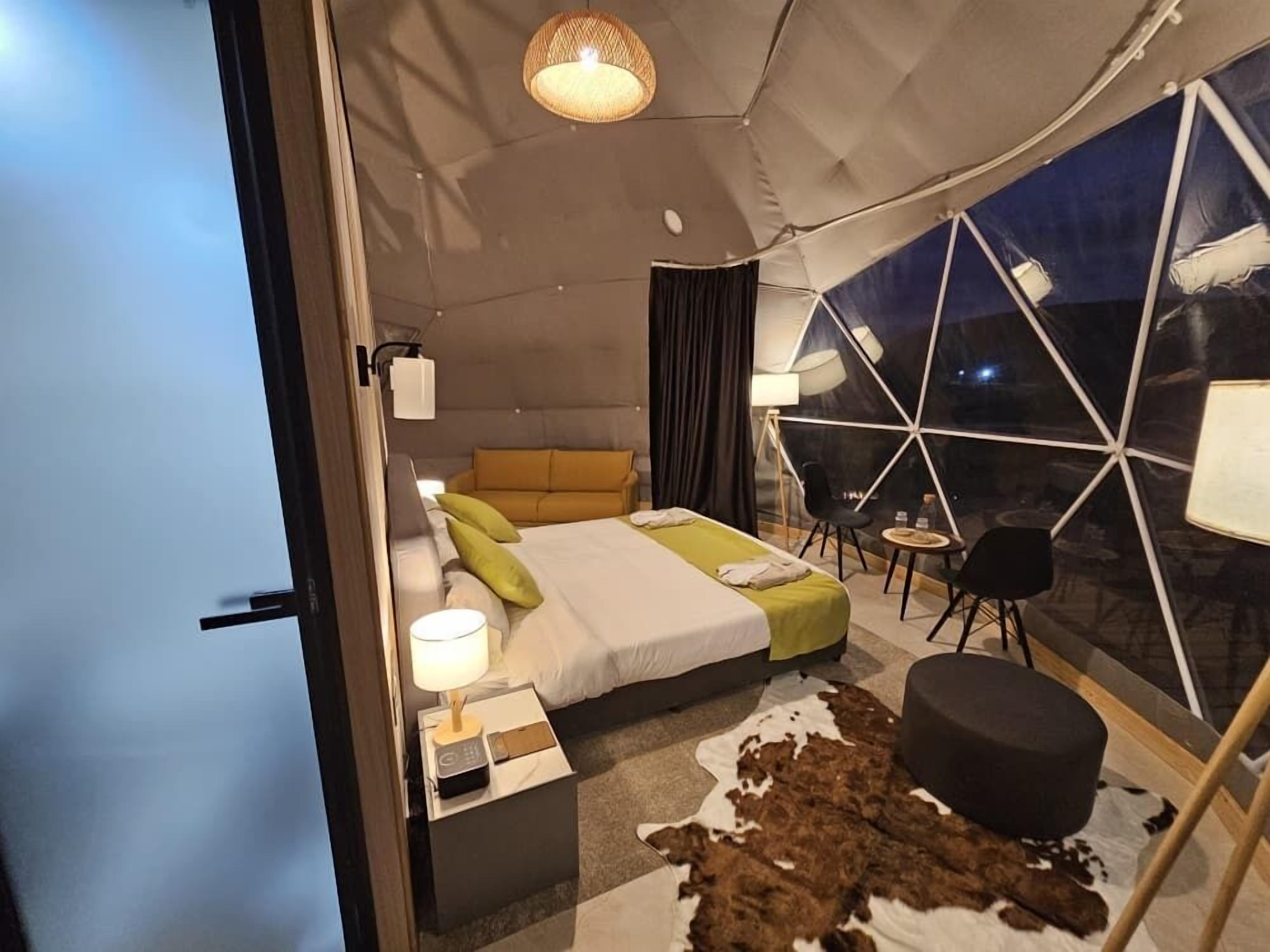 A modern bedroom with a bed, bedside table, lamp, and a view of the night sky through a geometric window.