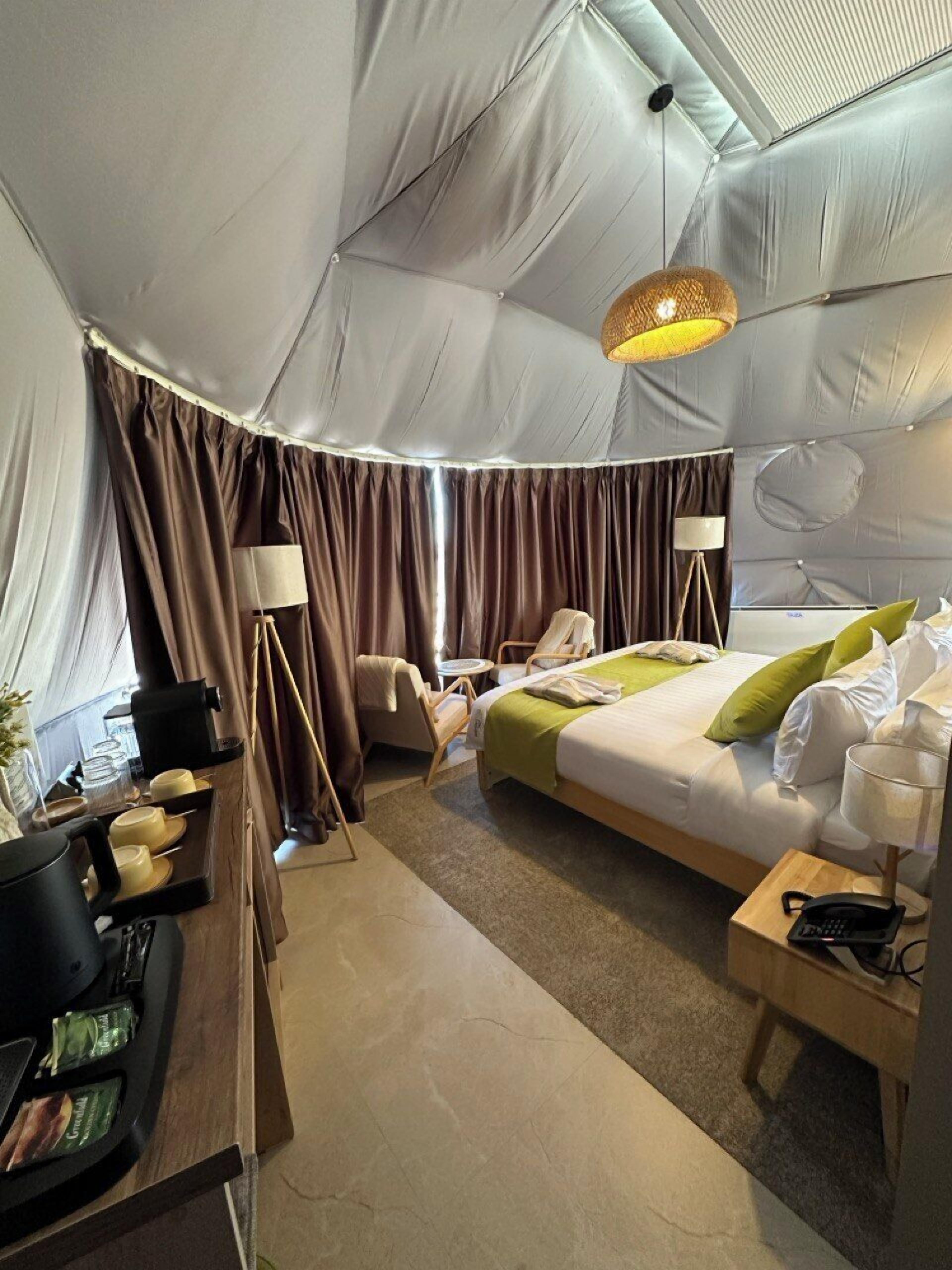 A tent-style room with a bed, bedside table, lamp, and a desk with a telephone.