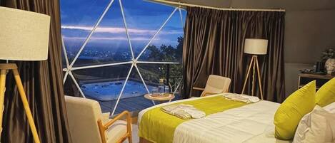 A tented room with a bed, a chair, a lamp, and a view of a landscape.