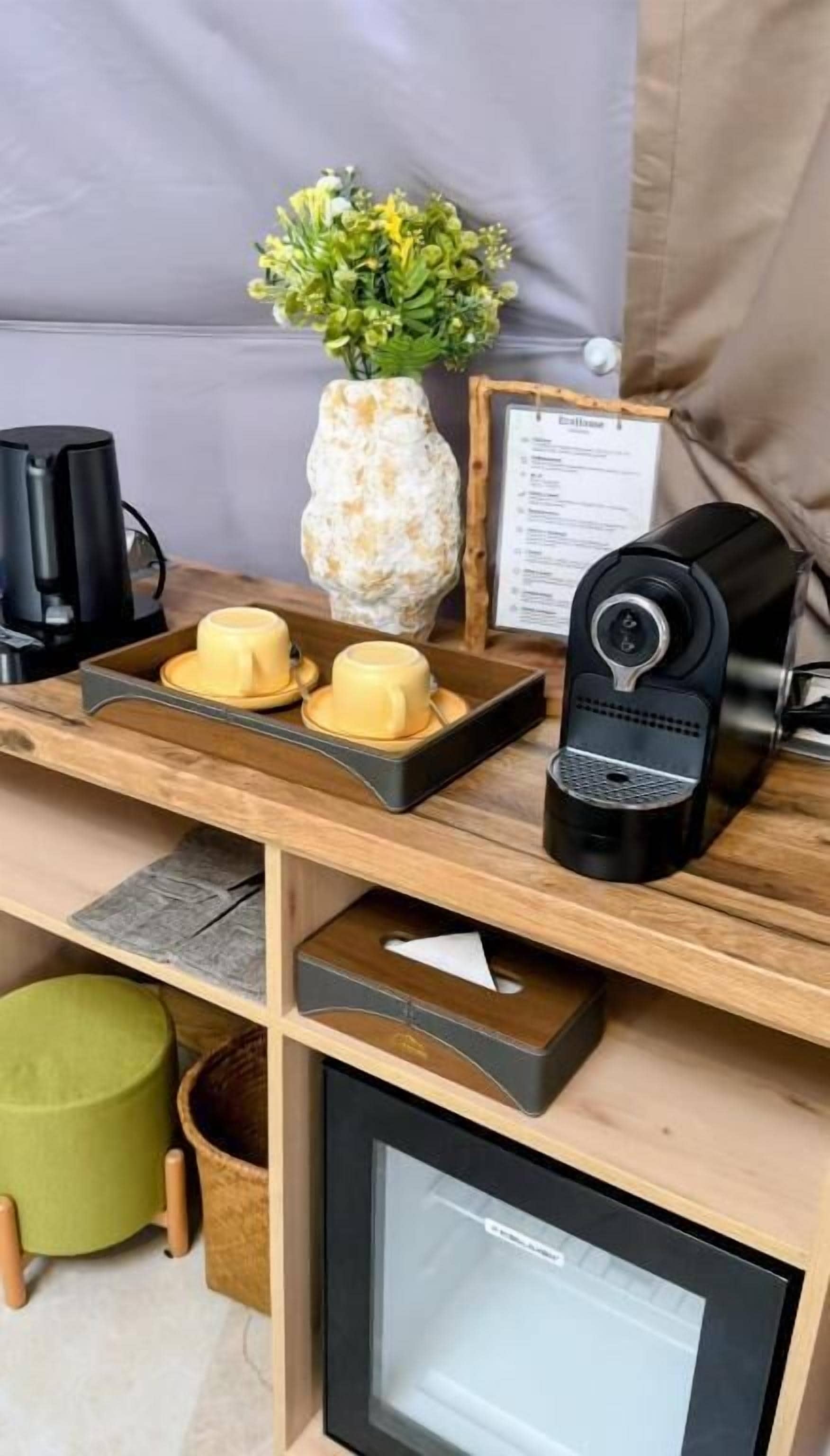 A wooden desk with a coffee maker, a vase with flowers, and a menu on a clipboard.