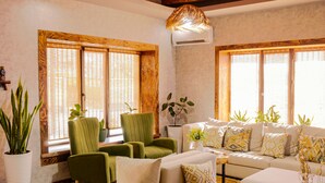 A living room with a wooden ceiling, a green armchair, a beige sofa, and a large window with blinds. - EcoHouse Glamping by ART HOTEL (Bishkek)